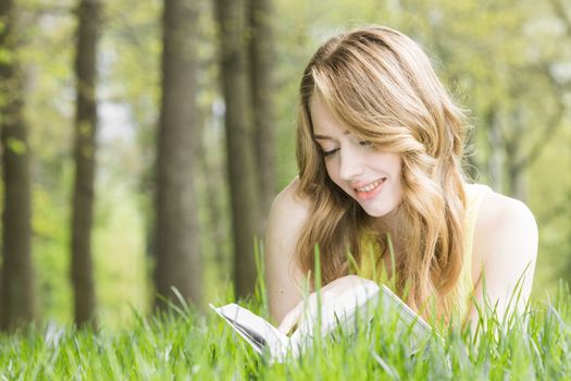Young beautiful woman lays on green grass field and reads book, spring exam concept, copy space for text
