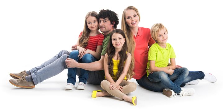 Happy smiling family of two parents and three children sitting on the floor studio isolated on white background