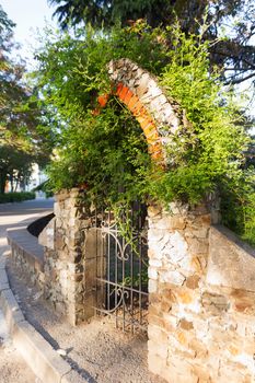 An ornate wrought iron gate in the stone wall of garden. Architecture detail. Crimea, Alushta. Russia.
