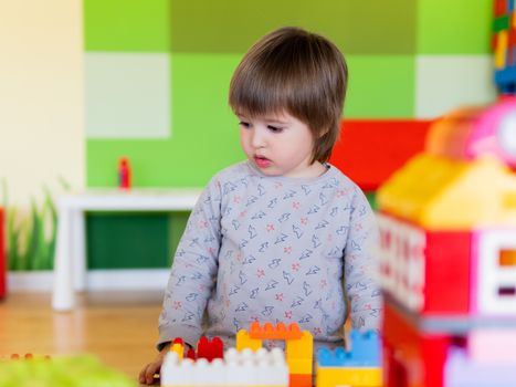 Toddler boy is playing in kidsroom with colorful constructor. Educational toy block in his hands. Kid is busy with toy bricks.