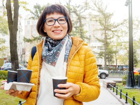 Happy wide smiling women in bright yellow jacketis holding paper cup with hot coffee. Hot beverage on cool autumn day.