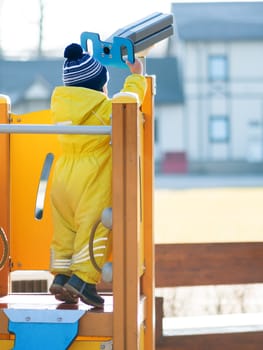 Toddler boy in yellow jumpsuit is playing on children playground. Child in bright clothes outdoor. Sunny autumn day.