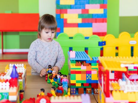 Toddler boy is playing in kidsroom with colorful constructor. Educational toy block in his hands. Kid is busy with toy bricks.