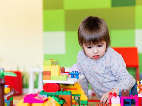 Toddler boy is playing in kidsroom with colorful constructor. Educational toy block in his hands. Kid is busy with toy bricks.