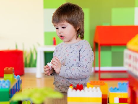 Toddler boy is playing in kidsroom with colorful constructor. Educational toy block in his hands. Kid is busy with toy bricks.