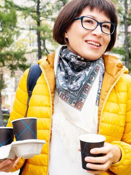 Happy wide smiling women in bright yellow jacketis holding paper cup with hot coffee. Hot beverage on cool autumn day.