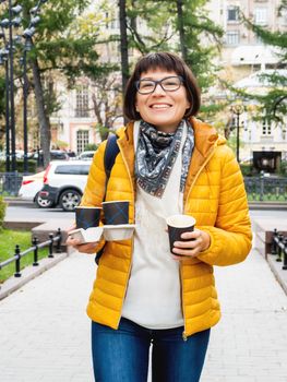 Happy wide smiling women in bright yellow jacketis holding paper cup with hot coffee. Hot beverage on cool autumn day.