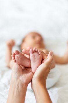 Mother holds newborn baby's bare feet. Tiny feet in woman's hand. Cozy morning at home.