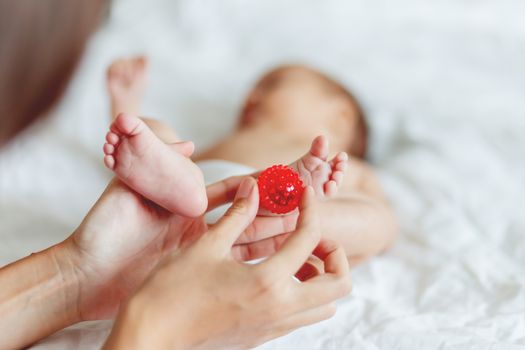 Mother holds newborn baby's feet. Tiny fingers and red massage ball in woman's hand. Cozy morning at home.