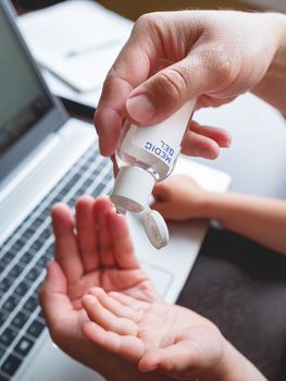 Self-isolation because of coronavirus outbreak. Man's hand with medical sanitizer gel for skin sterilization. Father is remote working with his little son.