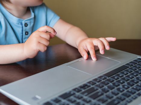 Curious toddler boy explores the laptop and presses buttons on computer keyboard.