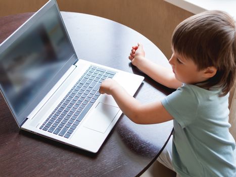 Curious toddler boy explores the laptop and presses buttons on computer keyboard.