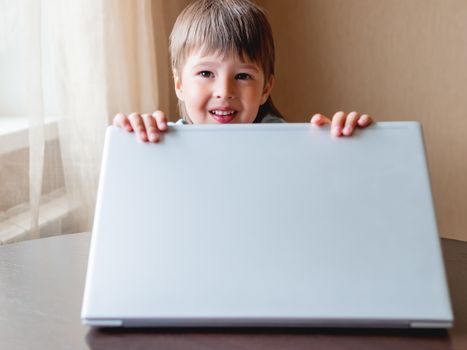 Curious toddler boy explores the laptop and smiles over screen of laptop.