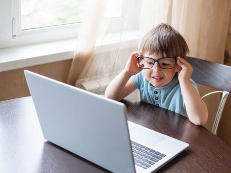 Curious toddler boy explores the laptop and staring on screen through big glasses. Symbol of online education for toddlers or impaired vision from prolonged exposure to screens of electronic devices.