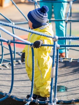 Toddler boy in yellow jumpsuit is playing on children playground. Child in bright clothes outdoor. Sunny autumn day.