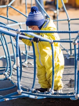 Toddler boy in yellow jumpsuit is playing on children playground. Child in bright clothes outdoor. Sunny autumn day.