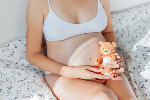 Pregnant woman in white underwear with toy bear. Young woman expecting a baby.