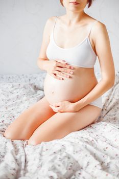 Pregnant woman in white underwear on bed. Young woman expecting a baby.