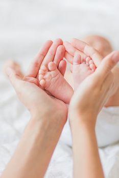 Mother holds newborn baby's bare feet. Tiny feet in woman's hand. Cozy morning at home.