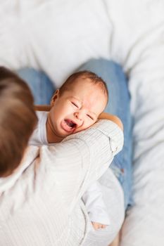 Woman holding a crying child. Mother comforts her little son or daughter. Baby with a big birthmark on his forehead.