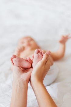 Mother holds newborn baby's bare feet. Tiny feet in woman's hand. Cozy morning at home.
