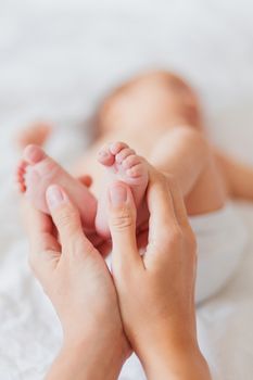 Mother holds newborn baby's bare feet. Tiny feet in woman's hand. Cozy morning at home.