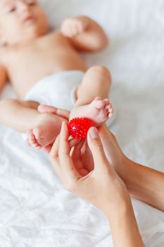 Mother holds newborn baby's feet. Tiny fingers and red massage ball in woman's hand. Cozy morning at home.