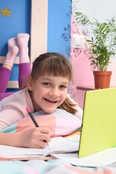 Happy schoolgirl studying at home lying in bed