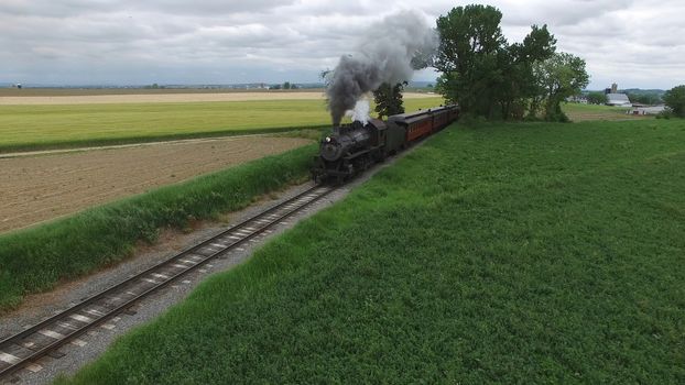 Aerial View of a Steam Passenger Train Puffing Smoke in Amish Countryside on a Sunny Spring Day