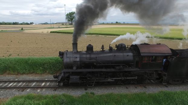 Aerial View of a Steam Passenger Train Puffing Smoke in Amish Countryside on a Sunny Spring Day