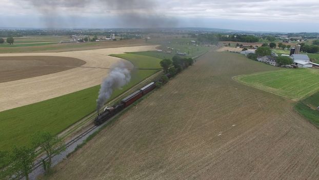 Aerial View of a Steam Passenger Train Puffing Smoke in Amish Countryside on a Sunny Spring Day