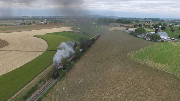 Aerial View of a Steam Passenger Train Puffing Smoke in Amish Countryside on a Sunny Spring Day