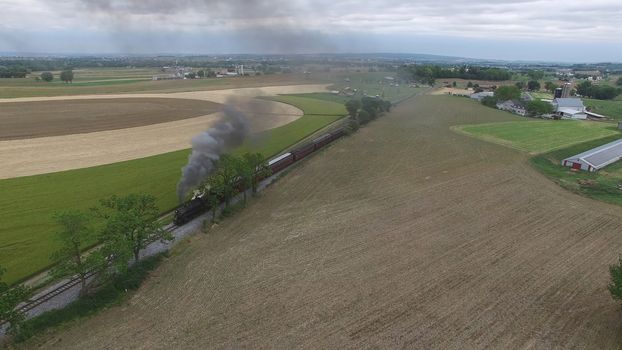 Aerial View of a Steam Passenger Train Puffing Smoke in Amish Countryside on a Sunny Spring Day