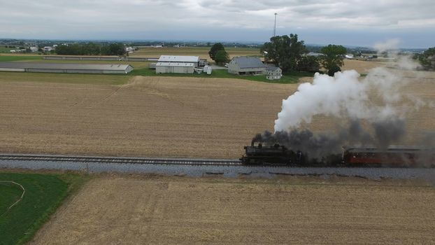 Aerial View of a Steam Passenger Train Puffing Smoke in Amish Countryside on a Sunny Spring Day