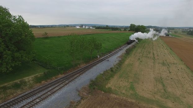 Aerial View of a Steam Passenger Train Puffing Smoke in Amish Countryside on a Sunny Spring Day