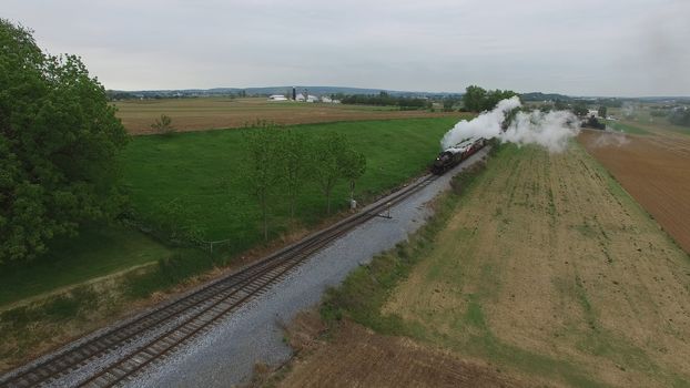 Aerial View of a Steam Passenger Train Puffing Smoke in Amish Countryside on a Sunny Spring Day