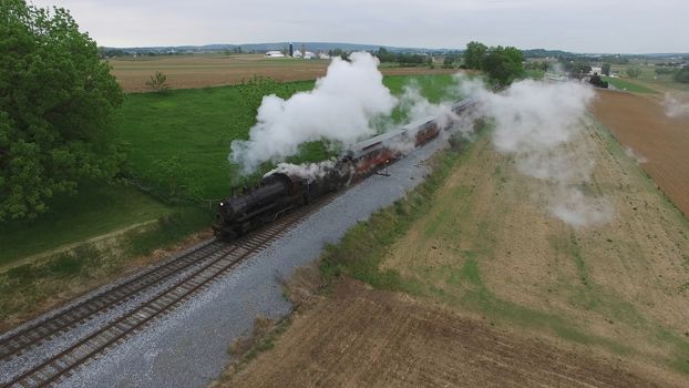 Aerial View of a Steam Passenger Train Puffing Smoke in Amish Countryside on a Sunny Spring Day