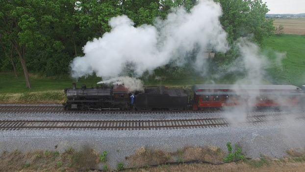 Aerial View of a Steam Passenger Train Puffing Smoke in Amish Countryside on a Sunny Spring Day