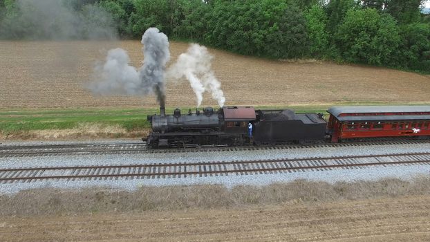 Aerial View of a Steam Passenger Train Puffing Smoke in Amish Countryside on a Sunny Spring Day