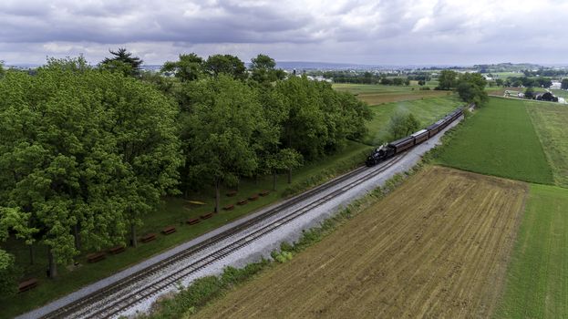 Aerial View of a Steam Passenger Train Puffing Smoke in Amish Countryside on a Sunny Spring Day