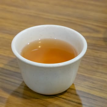 The close up of Taiwanese hot tea drink in white cup on wooden table.