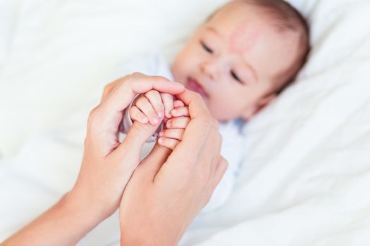 Mother holds newborn baby's hands. Tiny fingers in woman's hand. Cozy morning at home.