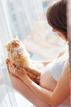 Pregnant woman in white underwear with cute ginger cat. Young woman expecting a baby. Risk of infection toxoplasmosis.