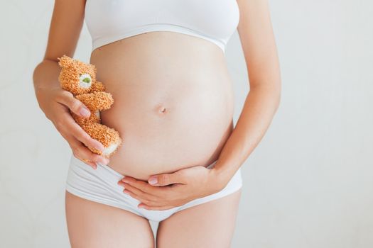 Pregnant woman in white underwear with toy bear. Young woman expecting a baby.