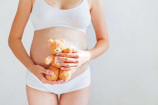 Pregnant woman in white underwear with toy bear. Young woman expecting a baby.