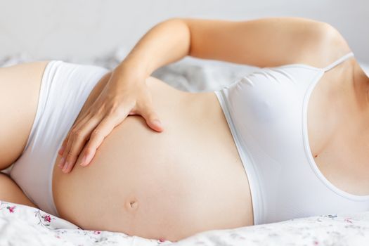 Pregnant woman in white underwear on bed. Young woman expecting a baby.