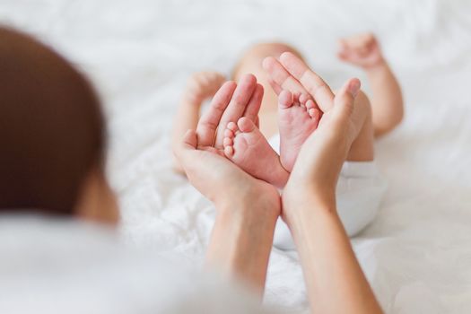 Mother holds newborn baby's bare feet. Tiny feet in woman's hand. Cozy morning at home.