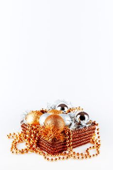 Golden and silver balls in box with tinsel and beads. Christmas and New Year decorations in woven box on white background. Copy space.