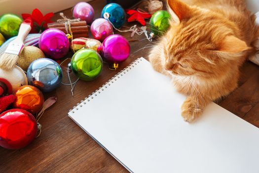 Cute ginger cat lying on clear paper page among Christmas and New Year decorations - bright colorful balls. Notepad paper for to-do-list or New Year promises.