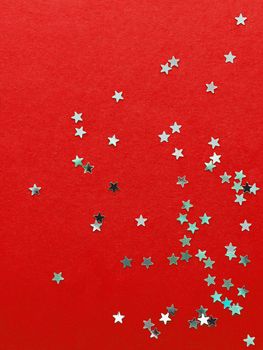 Holiday background with silver star confetti on red background. Good backdrop for Christmas and New Year cards.